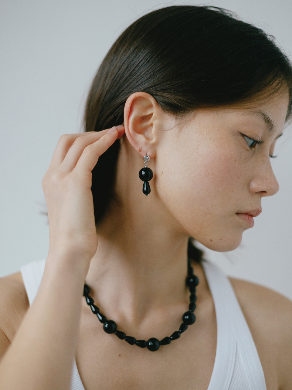 Woman wearing black beaded earrings and a necklace against a plain background